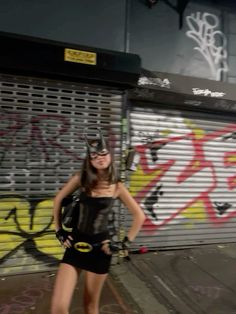 a woman standing in front of a graffiti covered wall with a batman mask on her head