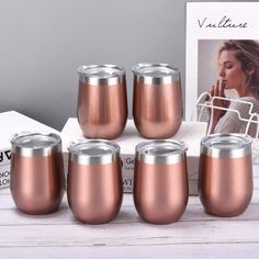 four copper colored tumblers sitting on top of a white table next to a magazine