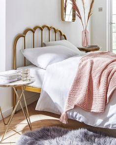 a bedroom with white bedding and gold headboard, pink throw blanket on the bed