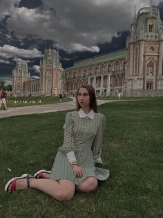 a woman sitting on the grass in front of a building with dark clouds above her