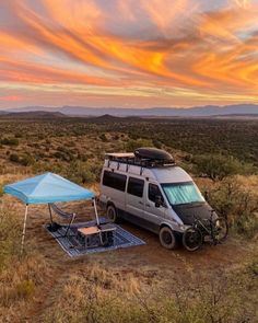 a van parked in the middle of an open field with a table and chairs on it