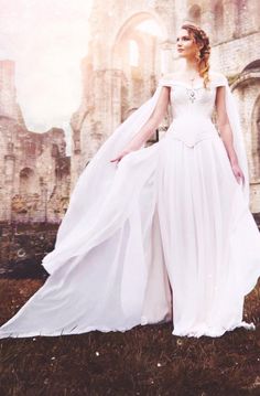 a woman in a white dress is standing near an old castle with her hands on her hips