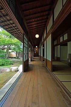 an empty hallway with wood flooring and large windows on both sides, surrounded by greenery