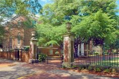 an iron gate in front of a brick building with trees on either side and sidewalk