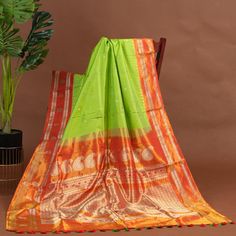 Vibrant as a tropical paradise, the parrot green Gadwal silk saree comes alive, gold zari woven orange temple border and pallu shimmering like sunrise on sacred waters. The orange blouse, a fiery complement, ignites the canvas. Together, they create a spectacle of joy, a celebration of life's vibrant hues. She who wears this saree is a goddess, her beauty and energy as radiant as the sun, her spirit as free as the wings of a bird. Every drape, every fold, tells a story of vitality, passion, and unbridled joy * Gadwal silk saree for special occasions. * Crafted from the premium quality fabric. * Supplied with a readymade blouse. * The blouse comes with an added allowance, and it can be altered to a standard size of 34"-42" on request. * Dry clean only to maintain colour and quality.  Note: Green Paithani Silk Pre-draped Saree With Self Design, Festive Green Paithani Silk Pre-draped Saree, Green Paithani Silk Pre-draped Saree For Diwali, Festival Green Paithani Silk Saree, Green Paithani Silk Saree For Festivals, Green Paithani Silk Pre-draped Saree With Unstitched Blouse, Green Self-design Paithani Silk Pre-draped Saree, Green Handloom Paithani Silk Pre-draped Saree, Green Saree For Rituals