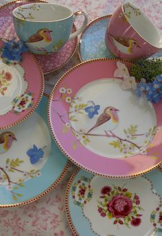 a table topped with plates and cups filled with flowers next to each other on top of a table cloth