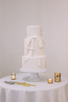 a white wedding cake sitting on top of a table next to candles and gold napkins