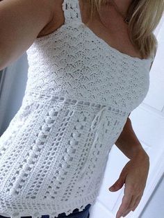 a woman is wearing a white crocheted top and has her hand on her hip