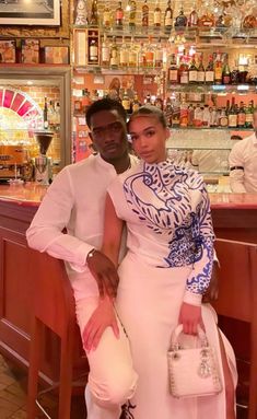 a man and woman standing in front of a bar with bottles on the wall behind them