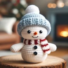 a small crocheted snowman sitting on top of a wooden stump in front of a fireplace