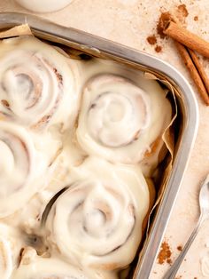 a pan filled with cinnamon rolls on top of a table next to some cinnamon sticks