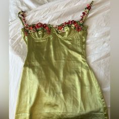 a green dress with flowers on it laying on a white sheeted bedding area