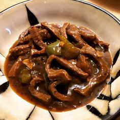 a white plate topped with beef and peppers covered in gravy on top of a wooden table