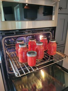 six jars of canned red peppers sit in an oven, with the door open and light on