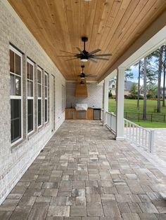 an outdoor covered porch with ceiling fan and windows on the side wall, surrounded by brick pavers