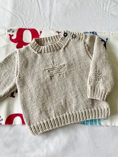 two knitted sweaters sitting on top of a white tablecloth covered in colorful elephant designs