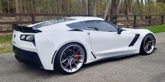 a white sports car parked on the side of the road in front of a wooden fence