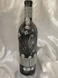 a black vase with white and silver designs on it's sides, sitting on a white cloth