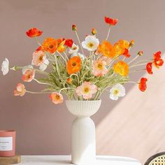 a white vase filled with lots of flowers on top of a table