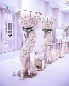 a row of tall vases filled with white flowers and candles sitting on top of a table