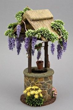 a miniature house with flowers and a potted plant in the corner on top of a stone wall