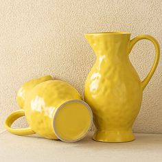 two yellow vases sitting next to each other on a table with a wall in the background