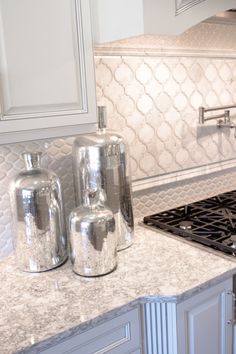 a white kitchen with marble counter tops and stainless steel stove top oven hood in the center