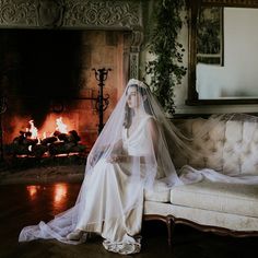 a woman sitting on a couch in front of a fire place wearing a wedding veil