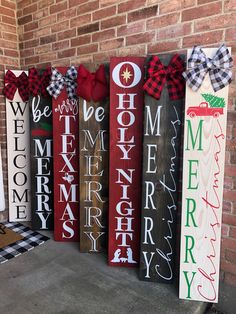 christmas signs are lined up in front of a brick wall with red and green bows