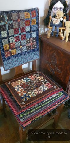 a stack of quilts sitting on top of a wooden chair next to a teddy bear