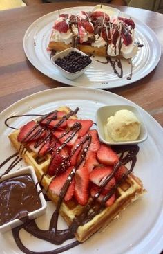 two white plates topped with waffles covered in chocolate sauce and strawberries next to ice cream