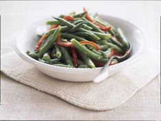 a white bowl filled with green beans on top of a cloth next to a spoon