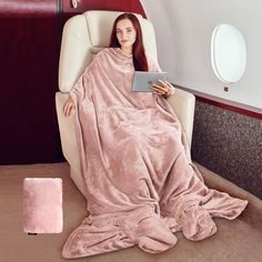 a woman is sitting in an airplane with a blanket on her lap and holding a tablet