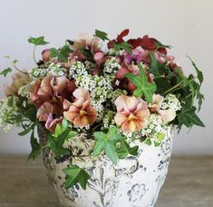 a white vase filled with lots of flowers on top of a wooden table next to a wall