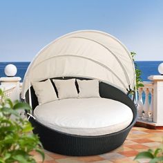 an outdoor day bed with white cushions on a tiled patio next to the ocean and blue sky