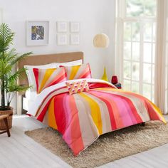 a bed with colorful comforters and pillows in a room next to a window on a rug