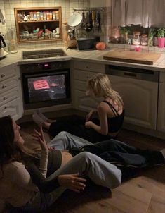 three women sitting on the floor in front of an oven and watching something on tv