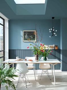 a dining room with blue walls, white chairs and flowers in vases on the table