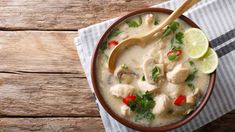 a bowl filled with chicken and vegetables on top of a napkin next to a wooden spoon