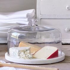 a cheese platter under a glass dome on a wooden table