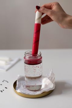 a hand is holding a red and white toothbrush in a glass jar on a table