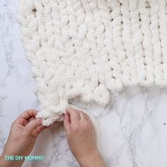 someone is crocheting a blanket on top of a marble surface with their hands