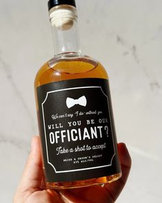 a person holding up a bottle of alcohol that says, will you be our officiant?