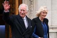 an older man and woman wave from the steps of a building while holding their hands in the air