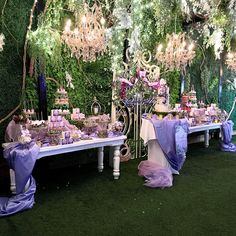 a table set up for a princess party with purple and white decorations on it, surrounded by lush greenery