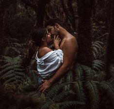 a man and woman kissing in the woods surrounded by fern trees, with their heads close to each other