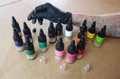 a person wearing black gloves and rubber gloves is holding an assortment of ink bottles in front of them