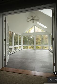 an empty room with large windows and a ceiling fan in the center, looking out onto trees