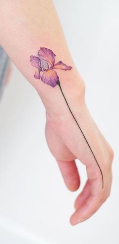 a woman's hand with a small purple flower tattoo on the left side of her arm