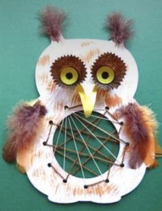 an owl made out of paper with yarn and feathers on it's face, sitting on a green surface